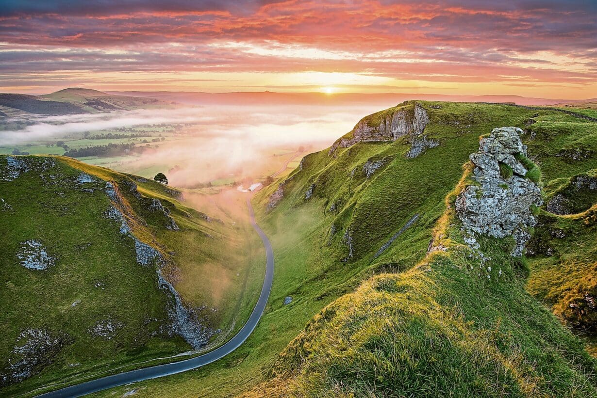 Long winding rural road leading into misty valley in the English Peak 